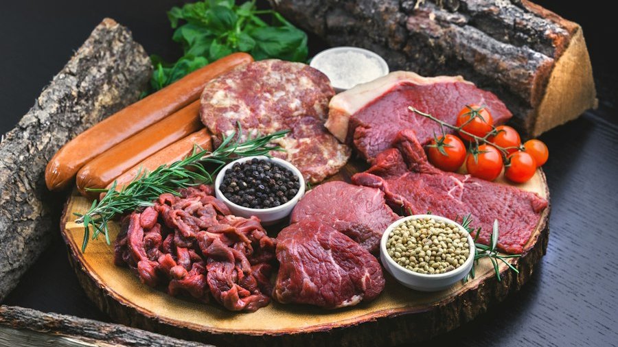Assorted raw meats, sausages, and spices on a wooden board with rosemary