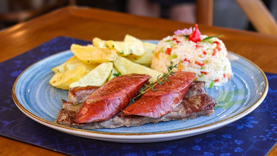 Close-up of a steak served with rice and potatoes on a decorated plate.