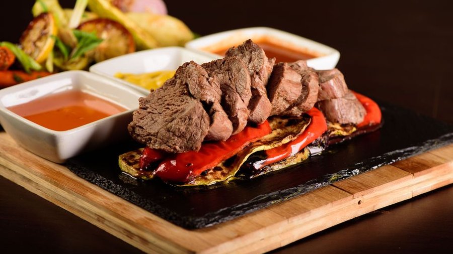 A delicious gourmet steak with grilled vegetables and various sauces. Perfectly styled for food photography.