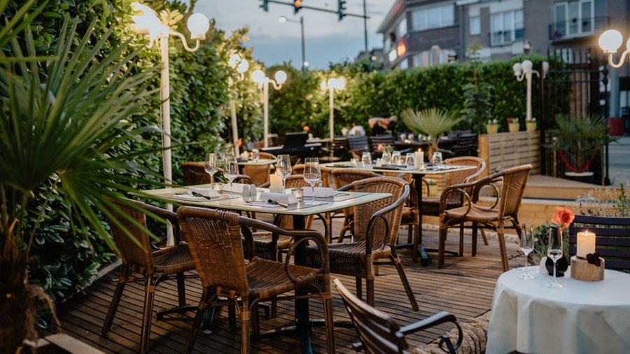 Terasă de restaurant cu mese pregătite, scaune din ratan și felinare aprinse la lăsarea serii